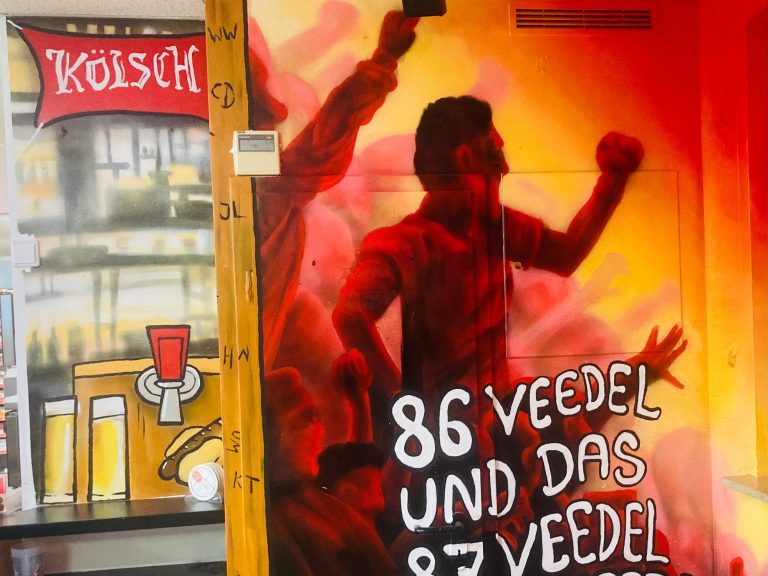 
Innenraum-Wandmalerei der bft Tankstelle Aegidienberg mit 1. FC Köln Fans und Spruch
