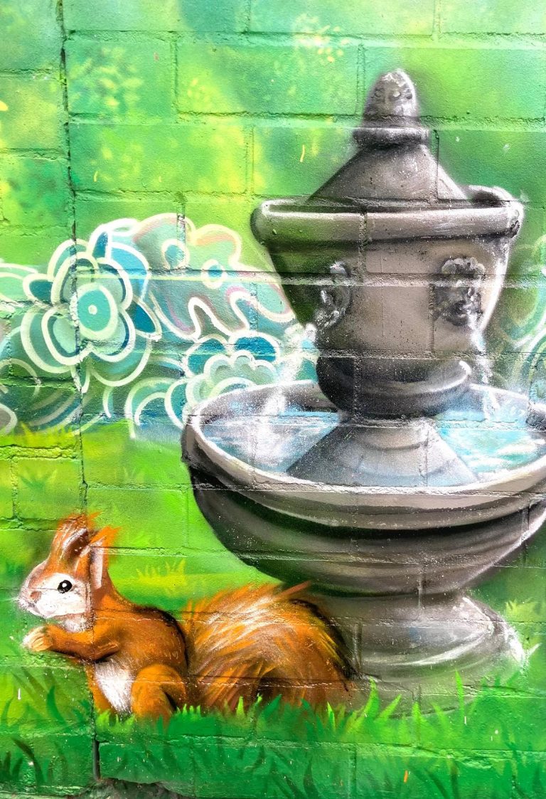 Farbenfrohes Graffiti mit Initialien auf einer Gartenwand in Sankt Augustin, kombiniert mit Eichhörnchen und Springbrunnen