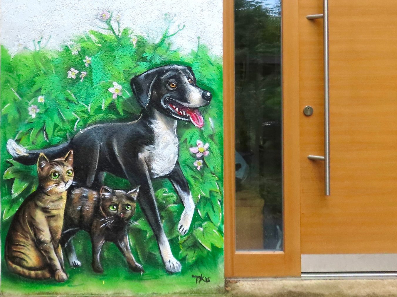 Graffiti Haustiere an einer Außenwand in Altfrauenhofen: ein schwarzer Hund und zwei Katzen am Eingangsbereich