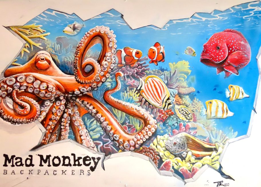 Großes Unterwasser-Graffiti mit orangefarbenem Oktopus, Fischen und Korallen im Innenhof des Mad Monkeys Waterfront Hostels in Cairns
