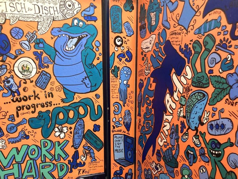 
Kabinentoiletten des Gymnasiums Schloss Hagerhof, komplett mit detailreichen orange-blauen Doodle-Illustrationen gestaltet
