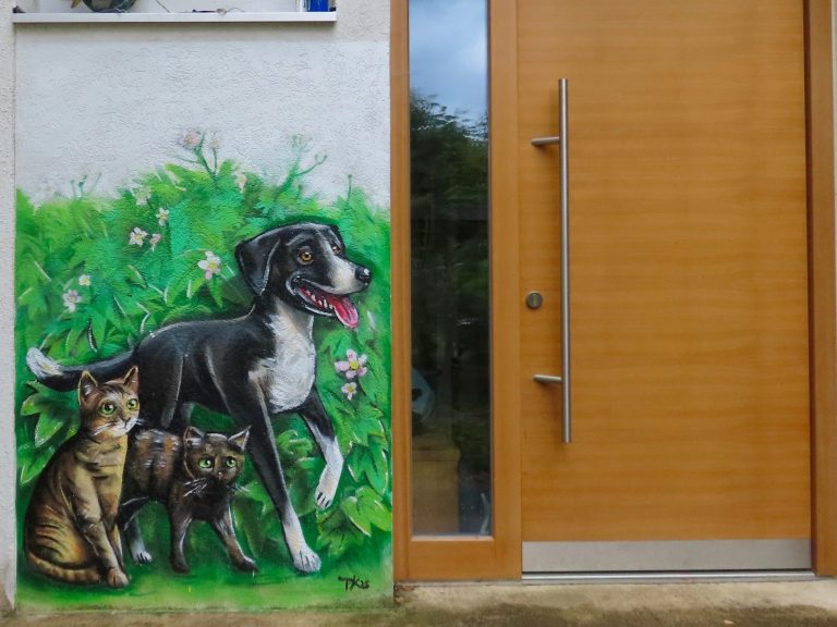 
Graffiti Haustiere an einer Außenwand in Altfrauenhofen: ein schwarzer Hund und zwei Katzen am Eingangsbereich
