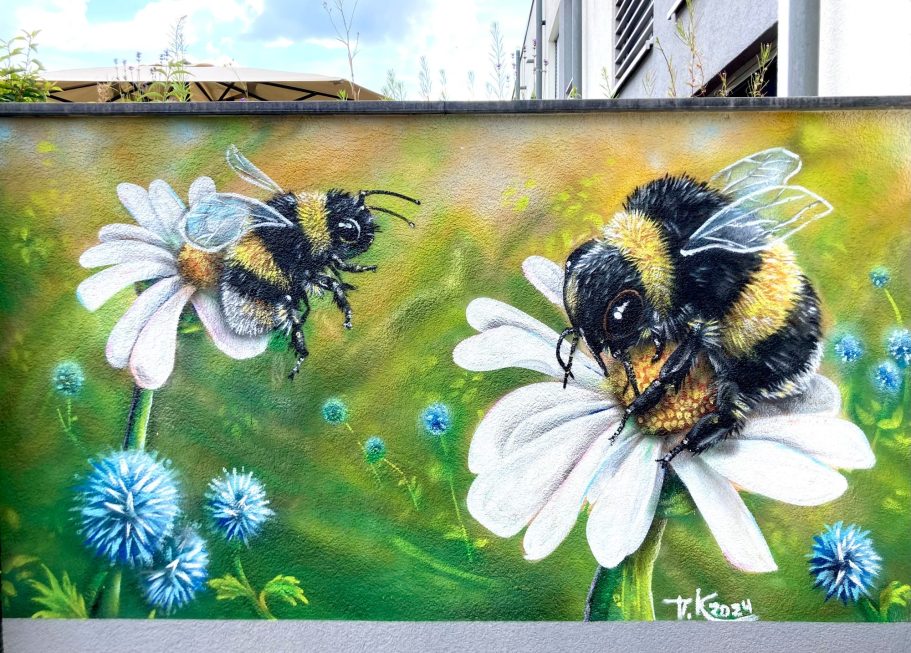 
Realistische Graffiti-Wandmalerei mit zwei großen Hummeln auf weißen Blüten vor grünem Hintergrund an einer Terrassenwand in Essen
